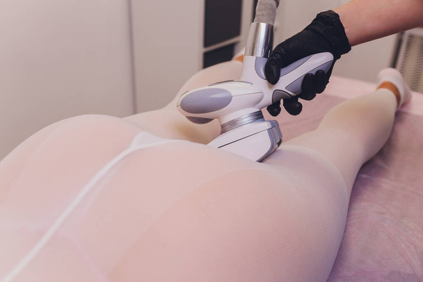 Частини жіночого тіла в спеціальному білому костюмі, що мають антицелюлітний масаж з спа-апаратом
. - Фото, зображення