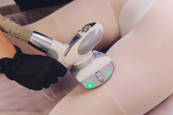 Parts of female body in special white suit having anti cellulite massage with spa apparatus. - Photo, Image