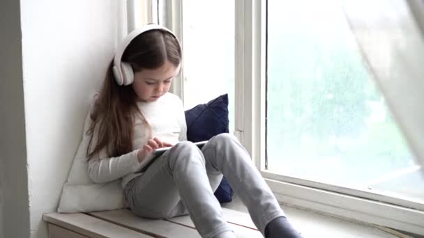 Sweet little girl, playing on tablet, sitting on a window shield. - Séquence, vidéo