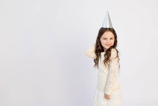 A cute little girl with a cap on a white isolated background is dancing and rejoicing. Space for text. Little girl celebrates birthday, holiday concept - 写真・画像