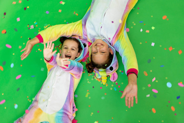 маленькі дівчата в яскравих костюмах лежать на зеленому ізольованому фоні зі стримером у яскравих однотонних костюмах. Простір для тексту. Концепція свята, День народження та продажів
 - Фото, зображення