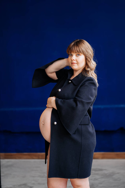 Γυμνή, όμορφη έγκυος με υπέρβαρο σε μπλε σακάκι. - Φωτογραφία, εικόνα