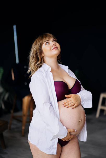 pregnant woman with overweight in underwear standing and stroking belly. - Foto, afbeelding