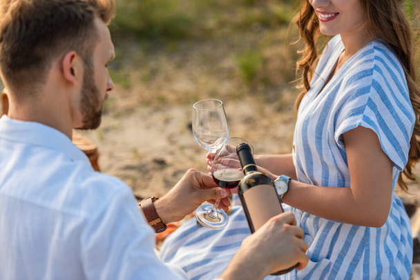 selektivní zaměření vousatý muž drží láhev při nalévání červeného vína ve skle blízko šťastná žena - Fotografie, Obrázek