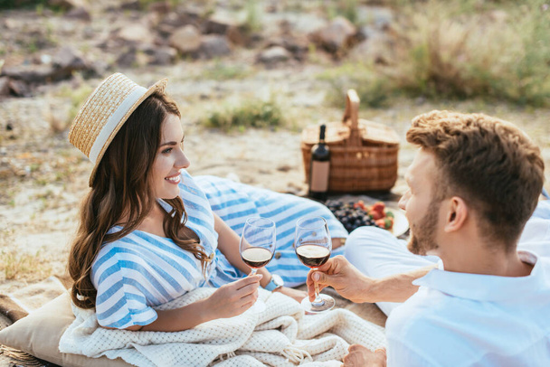 selective focus of happy woman in straw hat and bearded man holding glasses with red wine  - Fotoğraf, Görsel