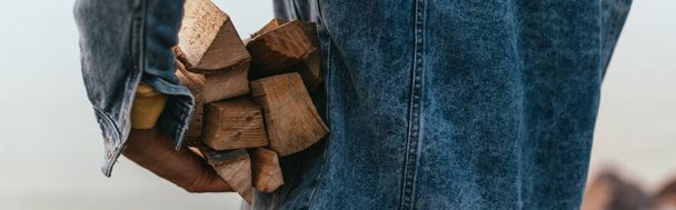 panoramic crop of man in denim jacket holding firewood  - Photo, Image