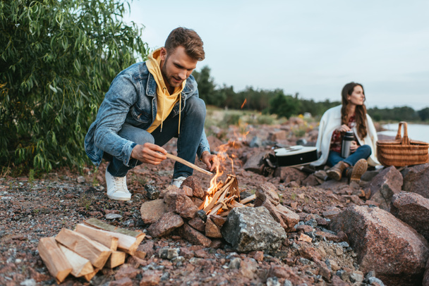 selective focus of handsome man holding stick near burning bonfire and woman  - Foto, immagini