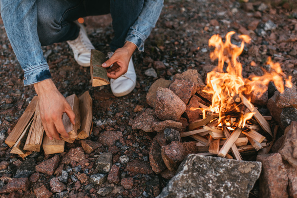 rajattu näkymä mies koskettaa puinen log lähellä polttava kokko - Valokuva, kuva