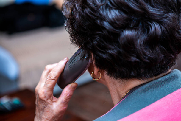 Koncentrálj a telefonra. A telefon egy idős nő kezében van, rövid fekete hajjal, és jelenleg is beszél. A kép hátulról készült.. - Fotó, kép