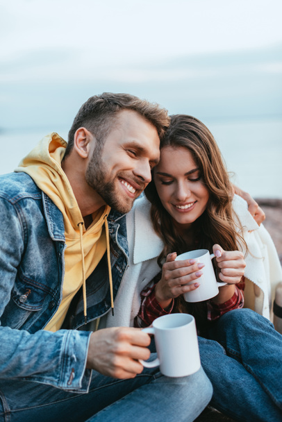 happy man hugging cheerful young woman and holding cup of tea - Foto, afbeelding