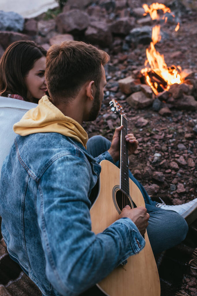 selective focus of bearded man playing acoustic guitar near girlfriend and bonfire - 写真・画像