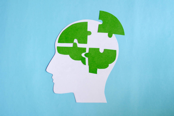 Zöld kirakós, mint emberi agy, kék háttérrel, memóriavesztés, demencia, Alzheimer-kór és mentális egészség koncepció. Papírvágás. - Fotó, kép