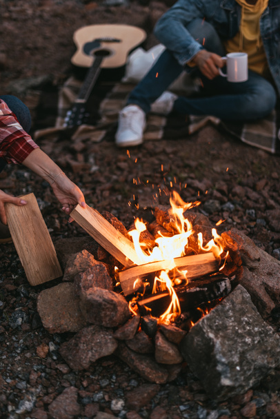 cropped view of woman putting log in burning bonfire - Fotografie, Obrázek