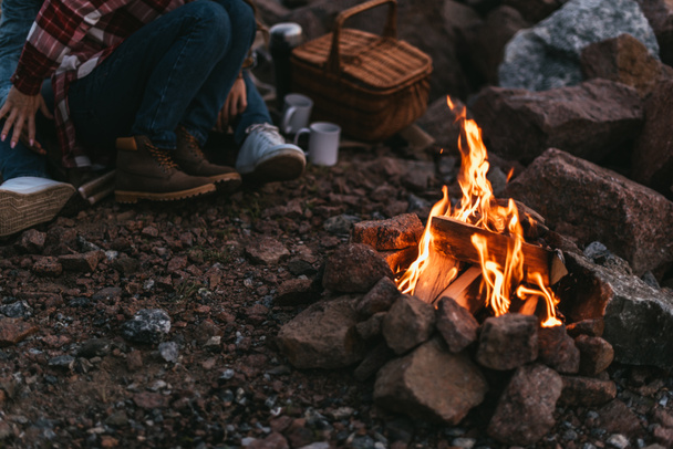 selective focus of burning bonfire near couple sitting on rocks - Fotografie, Obrázek