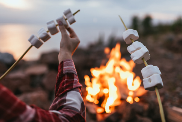 cropped view of couple holding sticks with puffy marshmallows near bonfire  - Foto, Imagem