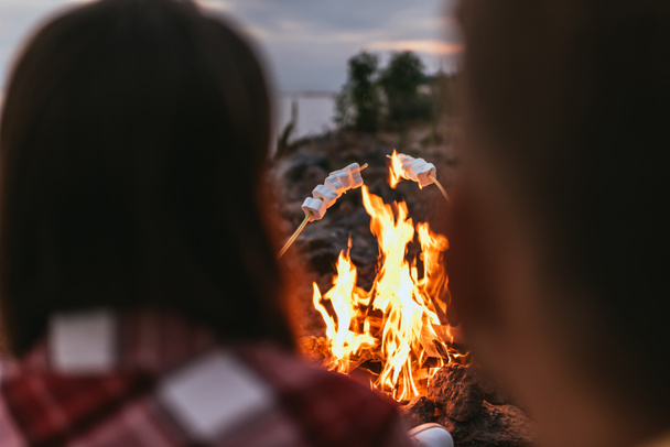 selective focus of puffy marshmallows on sticks near bonfire and couple - Photo, Image
