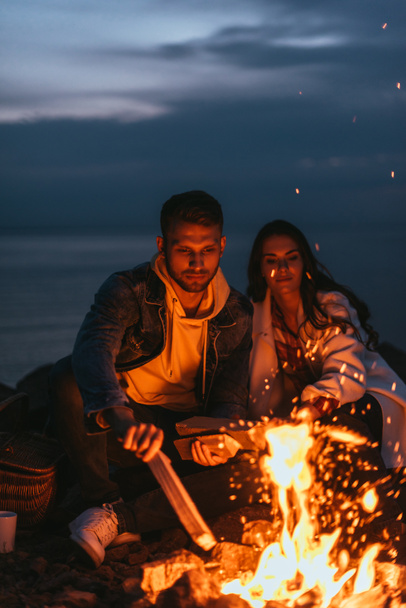 selective focus of handsome man putting log in bonfire near girl  - Photo, Image