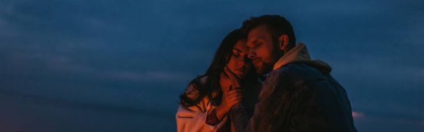 panoramic shot of bearded man touching attractive woman at night - Foto, afbeelding