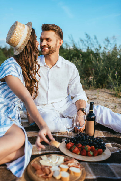 selective focus of happy couple sitting near tasty food and bottle with wine  - Fotoğraf, Görsel