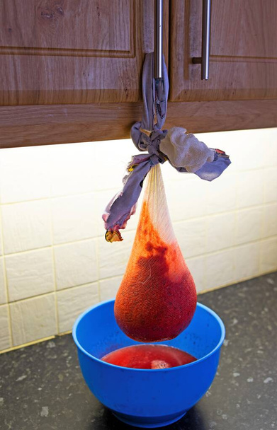 Pověšení mušelínové tašky na dveře kuchyňské skříně je jednoduchý a levný způsob, jak namáhat rozmačkanou směs potřebnou pro výrobu želé z červeného rybízu. - Fotografie, Obrázek