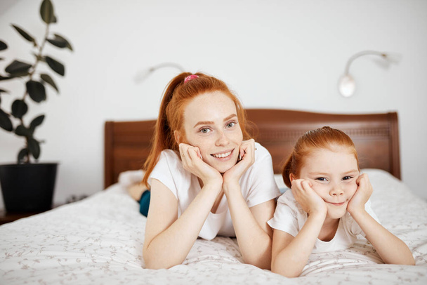 Mother and daughter enjoy in bed at home and looking at the camera. - Zdjęcie, obraz