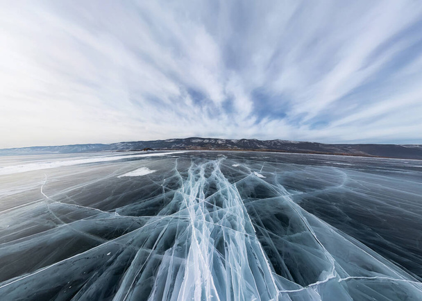 Ice of Lake Baikal in cracks near the island at sunset under gray clouds. Wide panorama - Foto, immagini