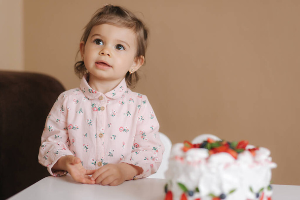 Cute little girl jeden i kadłub roku stoją przez pyszne ciasto urodzinowe. 18-miesięczna dziewczynka jest szczęśliwa i śmieje się. Wegetariańskie jedzenie. Bezglutenowe i wolne od laktozy. - Zdjęcie, obraz