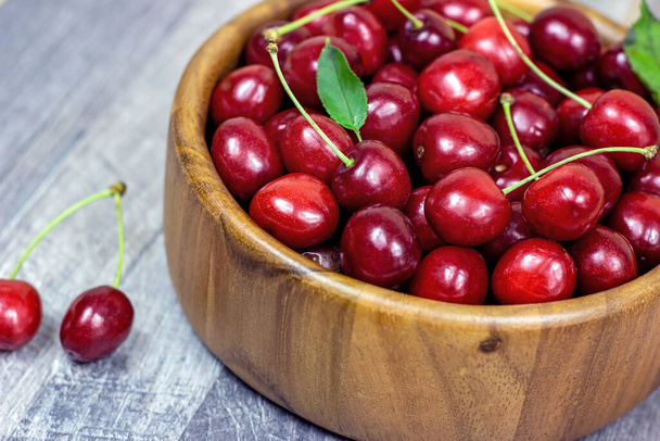 Свежие сочные красные сладкие вишневые ягоды в деревянной чаше на светлом фоне летом. - Фото, изображение