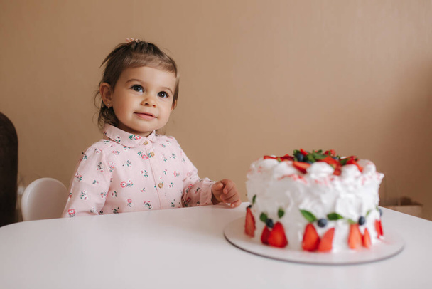 Χαριτωμένο κοριτσάκι ένα και ένα Χαλφ-year old σταθεί από νόστιμα τούρτα γενεθλίων. Δεκαοχτώ μηνών κορίτσι πολύ χαρούμενο και γελαστό. Χορτοφαγικό φαγητό. Χωρίς λακτόζη και χωρίς γλουτένη. - Φωτογραφία, εικόνα