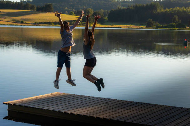 молодий чоловік і жінка стрибають з руками в повітрі, святкуючи успіх або початок свята.
 - Фото, зображення