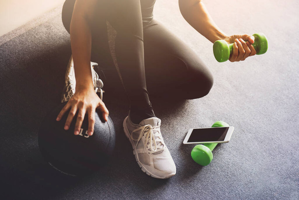 Sportliche Frau nutzt Smartphone beim Training zu Hause im Wohnzimmer.Online Personal Trainer oder am Handy .Sport- und Freizeitkonzept. - Foto, Bild