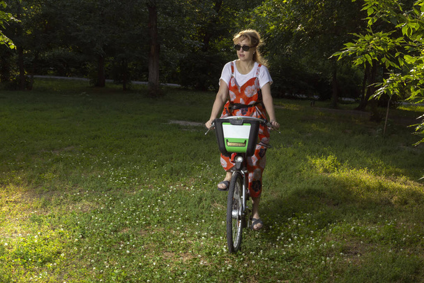Mature woman rides a bicycle in the evening park. Secluded walk - Photo, Image