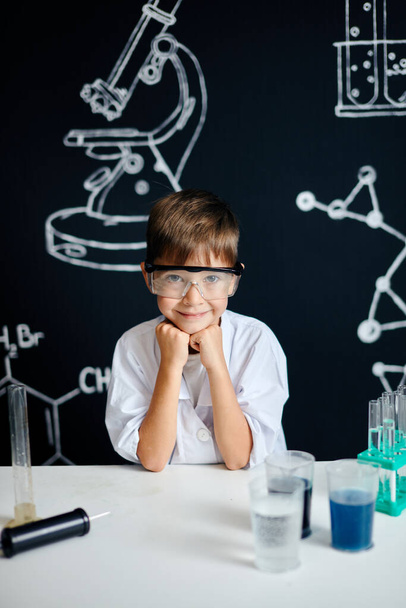 Little boy scientist in lab coat adjusting eyeglasses isolated on black - Foto, afbeelding