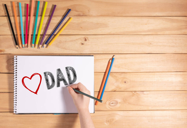 Child writing "LOVE DAD" on white sheet on wooden table - Photo, Image