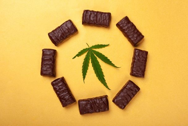 γλυκά με μαριχουάνα, κύκλος σοκολατάκια με φύλλο ιατρικής κάνναβη σε κίτρινο φόντο - Φωτογραφία, εικόνα