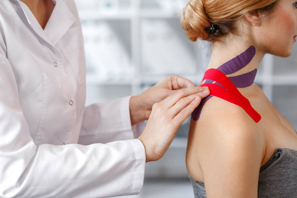 Kinesiology taping. Physical therapist applying kinesiology tape to patient neck. Therapist treating injured trapezius muscles of young athlete. Post traumatic rehabilitation, sport physical therapy - Zdjęcie, obraz
