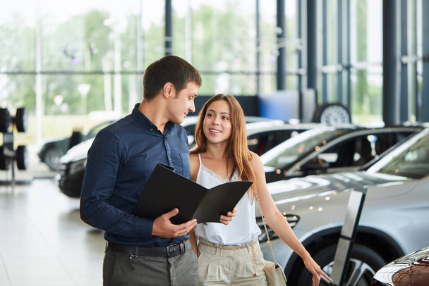Young couple in elegant summer time clothes choose a new car at car dealership - Foto, imagen