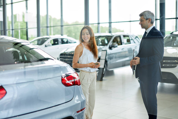Mladá žena zákazník žádá zralý sales manager, aby pomohl v prodejně automobilů. - Fotografie, Obrázek