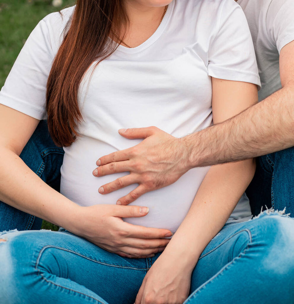 Mooie brunette zwangere vrouw in een wit T-shirt met haar man. Zwangere vrouw met geliefde man staan in de buurt van de rivier. Wachtende baby. Zonder gezichten. - Foto, afbeelding