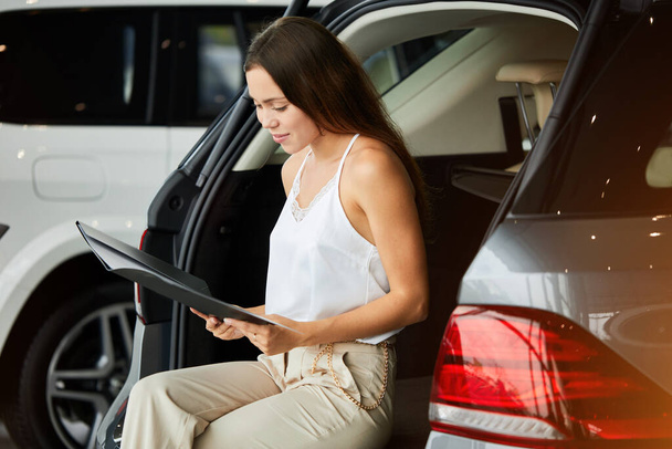 Smiling woman choosing new car at car showroom and reading properties - Foto, Bild