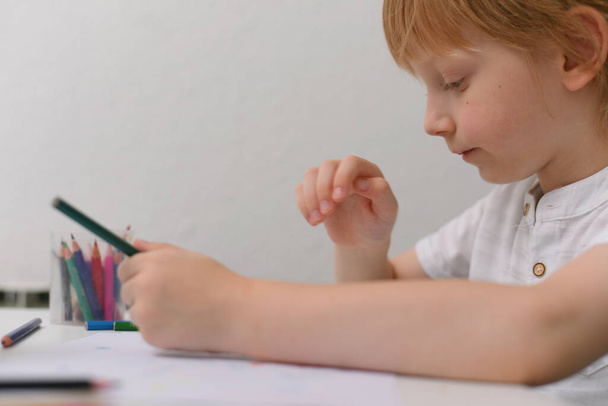 タブレットと描画ツールを持つ5歳の少年。学校の宿題をするデジタルタブレットやノートブックとの距離オンライン教育. - 写真・画像