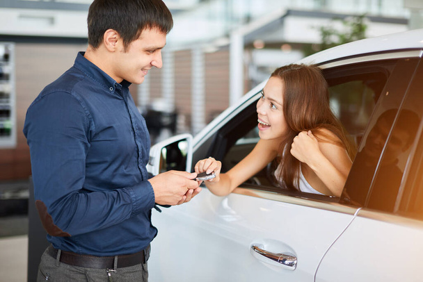 ar salesman giving car keys to young woman sitting in car in auto dealership - Fotoğraf, Görsel