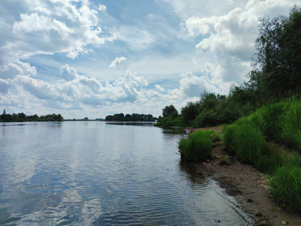 голубое облачное небо над зеленым берегом реки - Фото, изображение