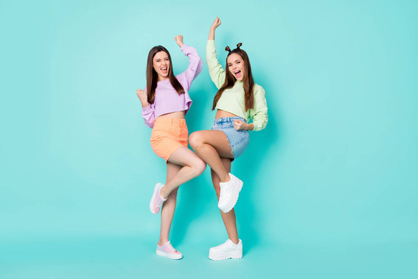 Full length photo of two cheerful ladies friends celebrate lottery winning cool look clothes wear cropped sweaters naked belly short skirts shoes isolated pastel teal color background - Zdjęcie, obraz