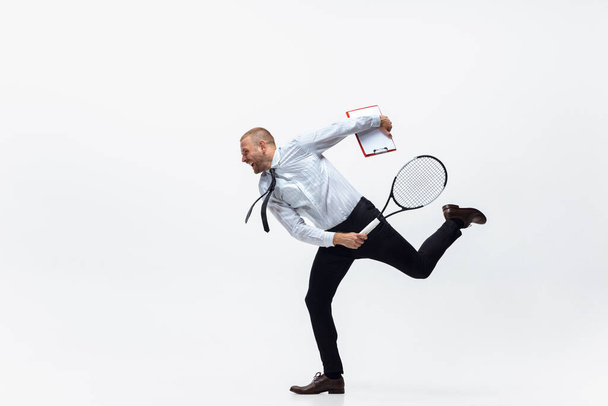 C'est l'heure du mouvement. Homme en vêtements de bureau joue au tennis isolé sur fond de studio blanc. - Photo, image