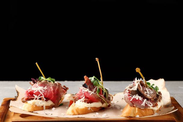 set of traditional spanish tapas with beef on wooden deck and black background. topas or bruschetta with beef and microgreen. - 写真・画像