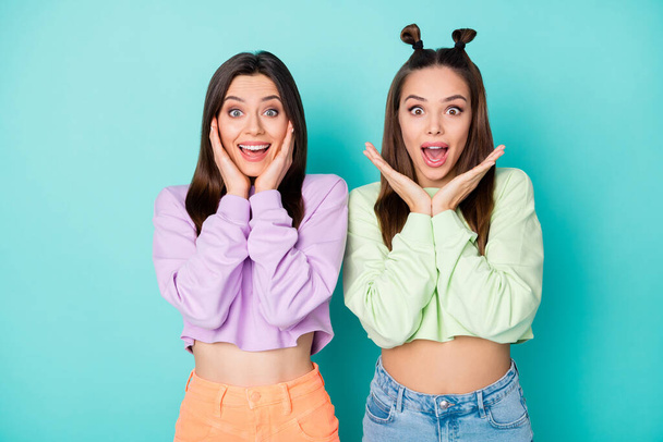 Photo of two pretty shocked lady friends cool youth look clothes listen good news arms near cheekbones wear cropped sweaters naked belly skirts isolated pastel teal color background - Foto, immagini