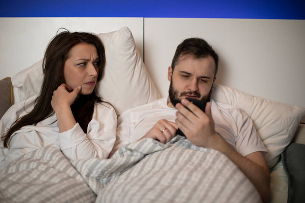 bruna ragazza a letto gelosamente guarda il suo fidanzato chattare con qualcuno - Foto, immagini
