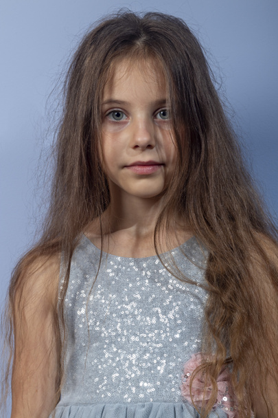 A beautiful long-haired girl with her favorite items in her hands on a light background in a gray dress with sequins. Foreground. Portrait shooting. Quarantine, games at home. - Фото, изображение