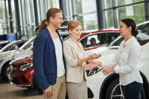 Happy young couple receiving car key from a salesman at the car dealership. - Fotografie, Obrázek